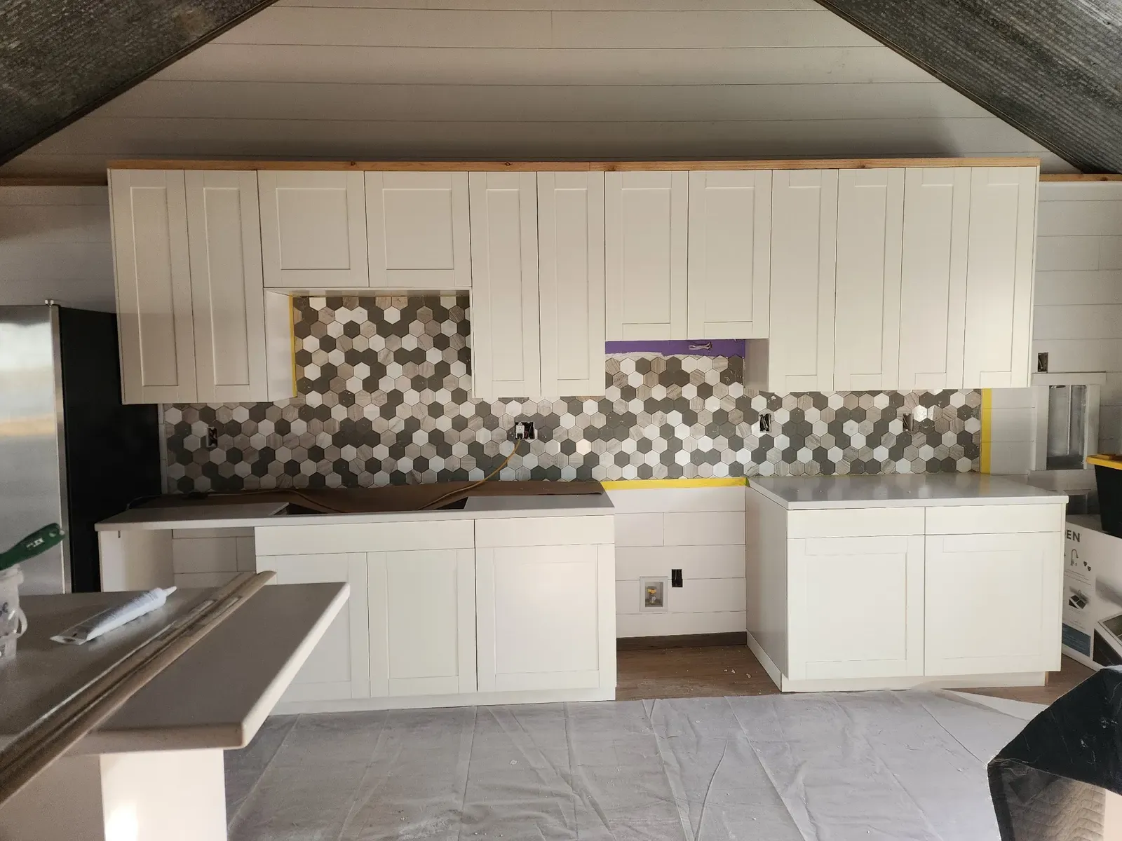 Hex tile backsplash being installed between the cabin kitchen cabinets