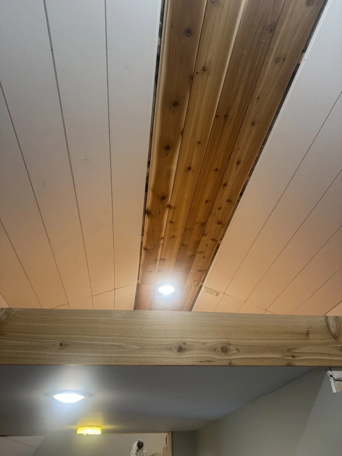 Finished white plank ceiling with a cedar accent strip and exposed wood beam