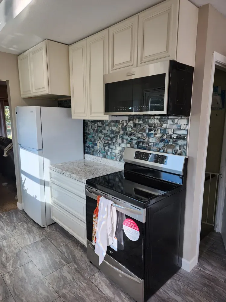 Wide view of the finished kitchen remodel with new flooring, white cabinets, mosaic backsplash, and new appliances