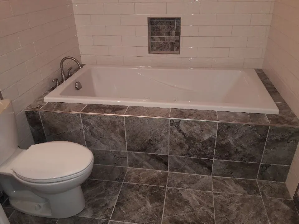 Finished basement bathroom with tiled floor and tub surround