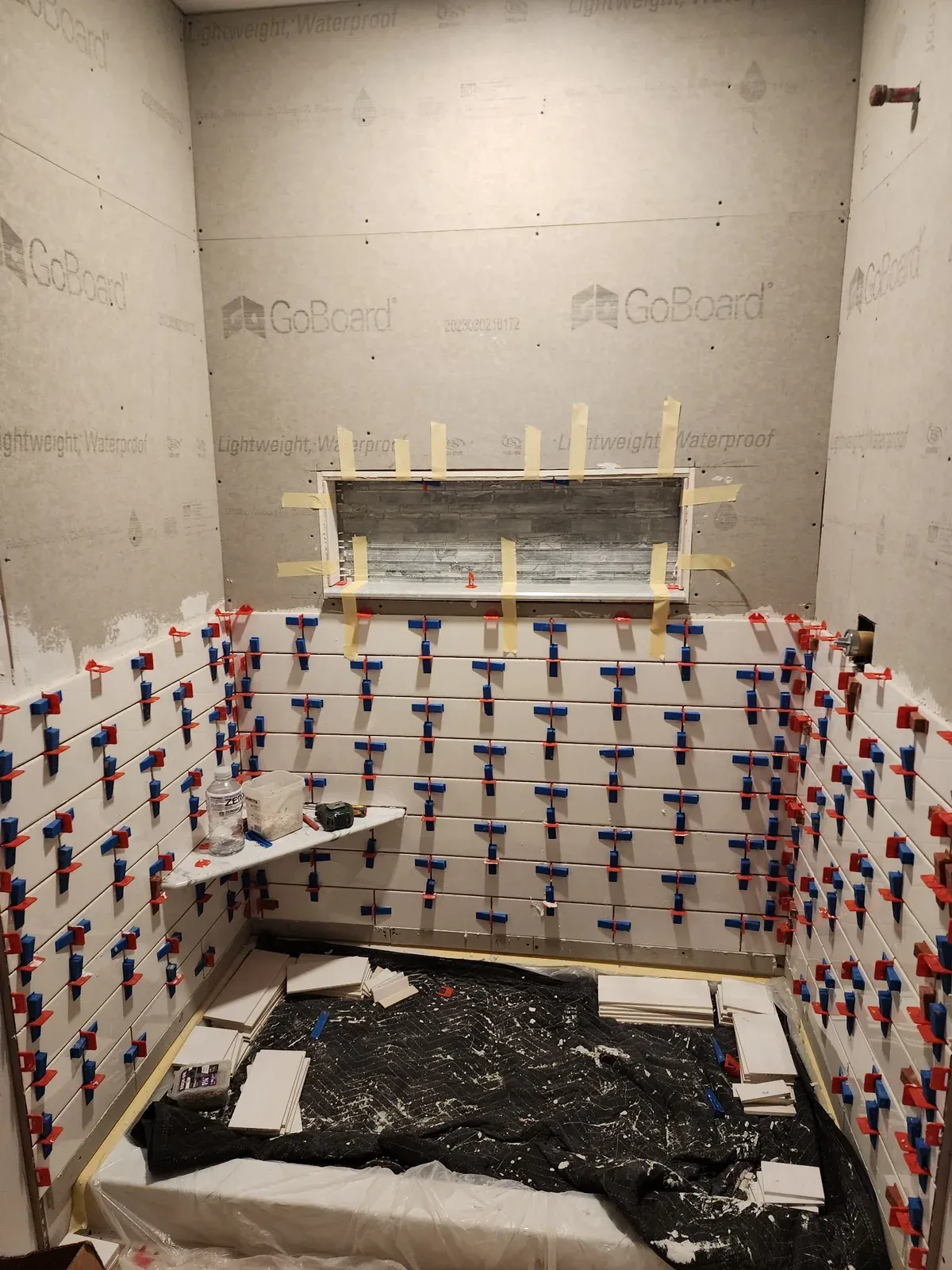White subway tile being installed with leveling spacers around the shower niche