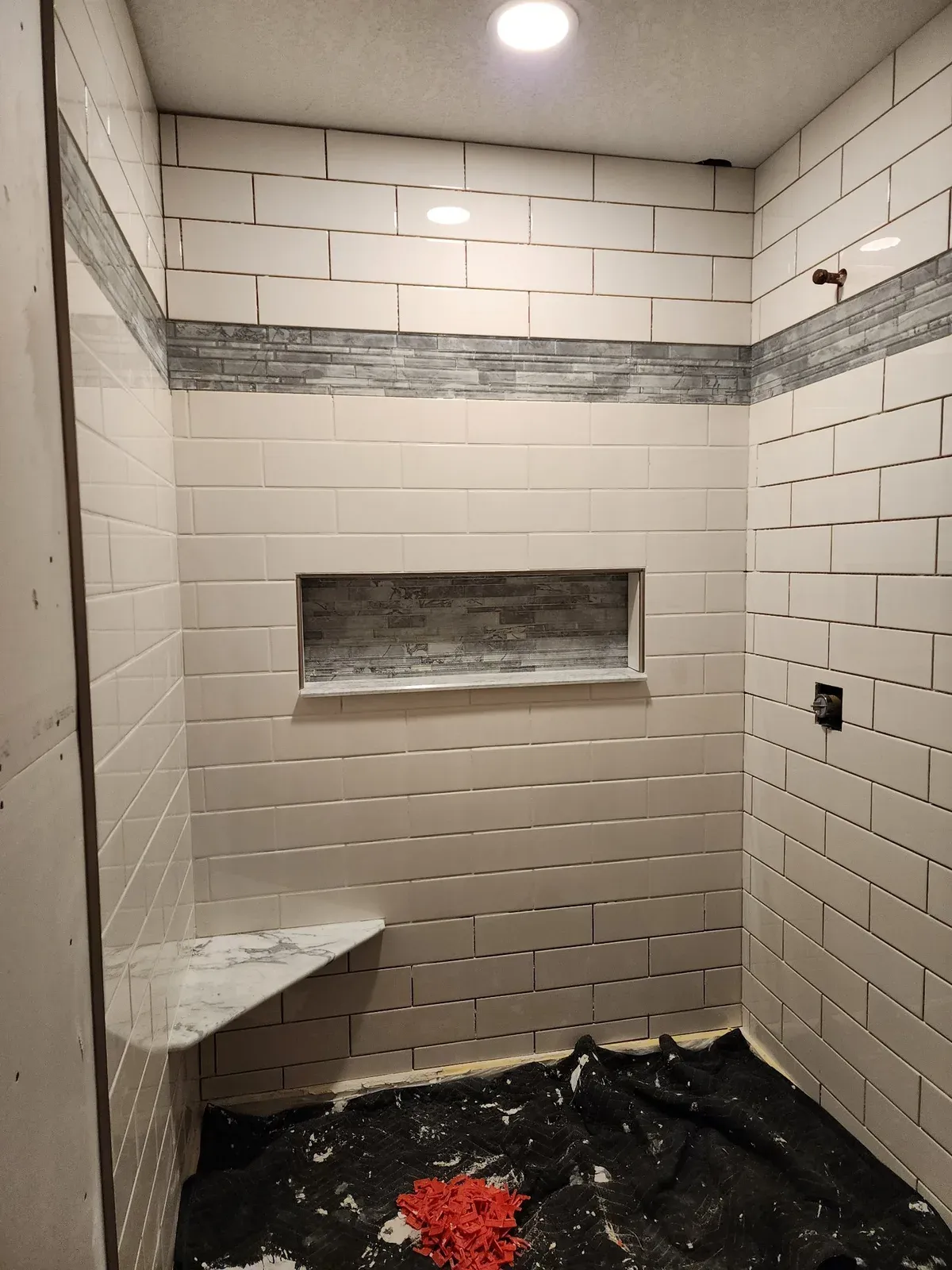 Walk-in shower with subway tile, mosaic accent band, niche, and bench while the floor is still protected for work